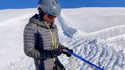 Person with helmet and ski goggles holding ski poles in the snow-covered mountains.