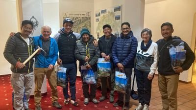 A group of eight people in casual clothing is standing in an indoor space with maps on the wall.