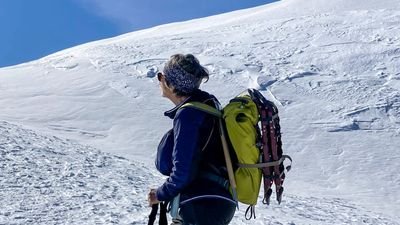 Person with backpack and hiking poles on a snow-covered mountain, wearing a headband and sunglasses.