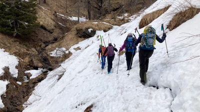 People with backpacks and sticks are hiking on a snow-covered mountain path.