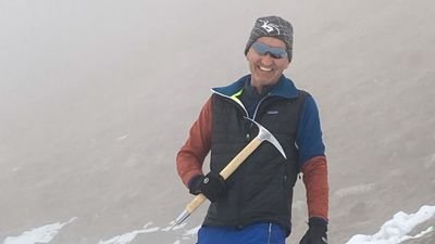 Person with ice pick and cap standing on snow-covered mountain in foggy surroundings.