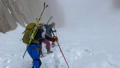 People with skis and poles are ascending in snow-covered mountain terrain.