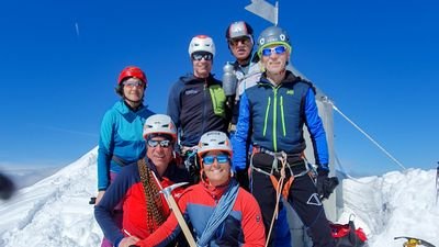 Group of people with helmets and climbing equipment on a snow-covered mountain peak.