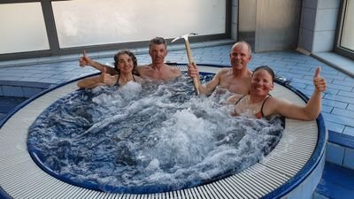 Four people in a hot tub, one holding an ice pick. All are giving a thumbs up.