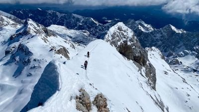 Mountaineers with helmets and ropes on a snow-covered ridge in an alpine mountain landscape.