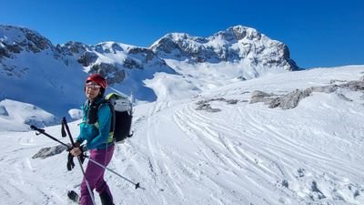 Person with helmet and ski poles on a snow-covered mountain against a rocky backdrop.