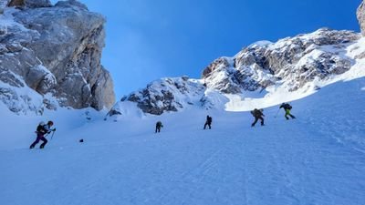 People with ski equipment are skiing down a snowy mountainside surrounded by rocks.