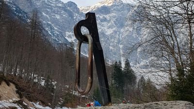 People in climbing gear with helmet and rope in a mountainous, wooded landscape.