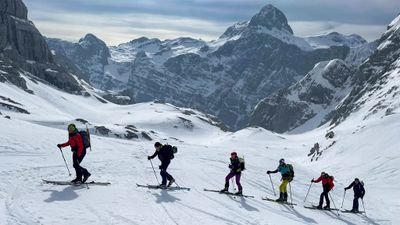 People with skis and backpacks are hiking in snowy mountains.