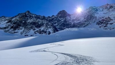 Traces in the snow in front of a mountain backdrop with bright sunshine and clear sky.