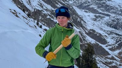 A person in winter clothing with an ice pick in a snowy mountain landscape.