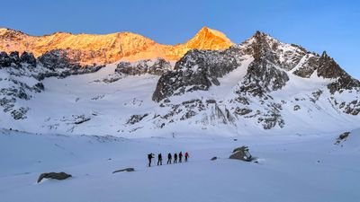 Group of people with skis and poles in snowy mountains at sunrise.