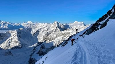 Mountaineers with helmets and climbing equipment on a snow-covered mountain path in the Alps.