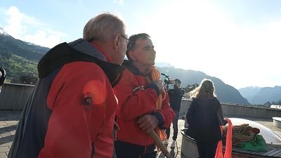 People in red jackets with ropes on a terrace in the mountains.