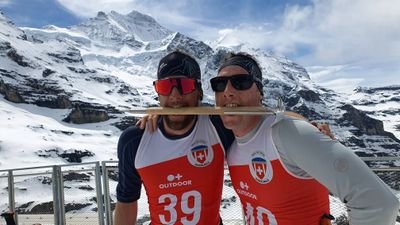 Two people in sportswear with headbands and sunglasses in front of snow-covered mountains.