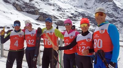Six people in ski clothing and helmets posing in front of snow-covered mountains.