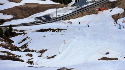 Skiers on a snow-covered slope in the mountains, wearing helmets and ski equipment, near a road.