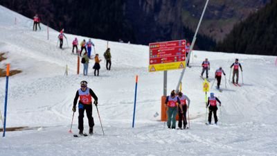 People with skis and helmets on a snowy slope, red starting numbers, information signs in the background.