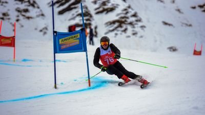 Skier with helmet and starting number slaloms on a snow-covered slope in the mountains.