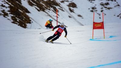 Two skiers wearing helmets and race numbers are skiing down a snow-covered slope.
