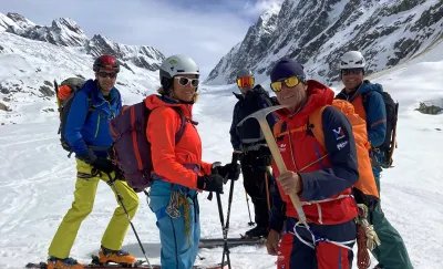 Five people with helmets and skis in snowy mountains, one person is holding an ice pick.