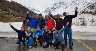 Group of people in winter clothing posing on a street in front of snow-covered mountains.