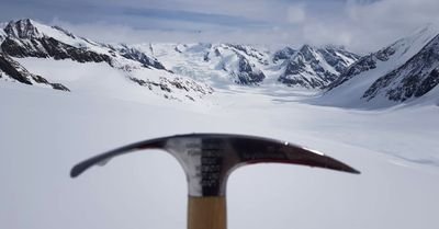 Ice pick in front of a snow-covered mountain landscape with glaciers and cloudy sky in the background.