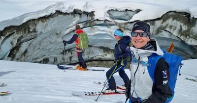 People with skis and helmets are standing in front of a crevasse in snow-covered mountains.
