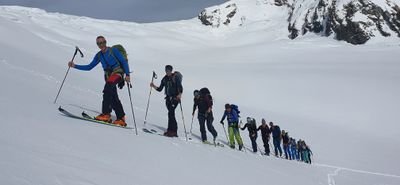 Group of people ski touring in snowy mountains, with ski poles and backpacks.