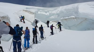 Group of people with hiking poles and backpacks on a snowy glacier.