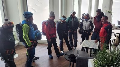 A group of people with helmets and backpacks is standing in a room, looking at a map.