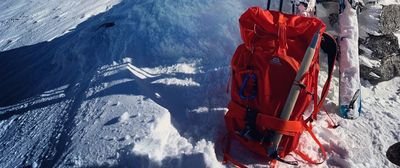 Red backpack with ice pick and skis on snow-covered mountain.