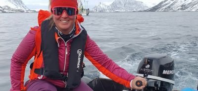 Person in boat with life jacket and cap is steering motorboat on the lake, surrounded by snow-covered mountains.