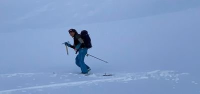 Person with a backpack and ice pick hiking in the snow. Wearing winter clothes and a hat.
