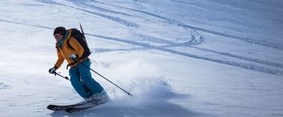 Person on skis with a helmet and backpack is skiing down a snowy mountain slope.
