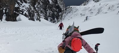 People with skis and helmets are climbing in the snowy mountain terrain.