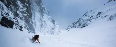 Person skiing in a snow-covered mountain valley, wearing a helmet and ski equipment.
