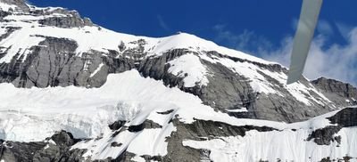 Snow-covered mountain landscape with rock walls and glaciers under a blue sky.