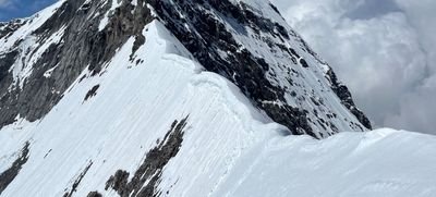 Snow-covered mountain peak in the Alps with steep rock walls and clouds in the background.