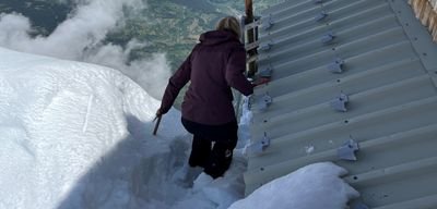 Person on snow-covered mountain next to cabin, holding onto railing.