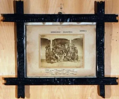 Old photo in a black frame shows a group of people with hiking sticks in front of a building.