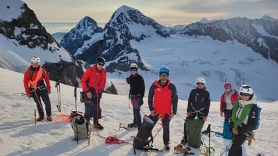Group of mountaineers with helmets and climbing equipment on a snow-covered mountain peak.