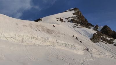 People with climbing equipment are climbing a snow-covered mountain.
