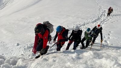 Group of climbers with helmets and ice axes climbing in the snow on a mountain.