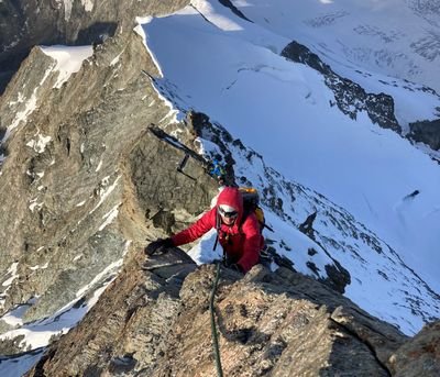 Climber with helmet and rope on a snow-covered mountain ridge in the Alps.