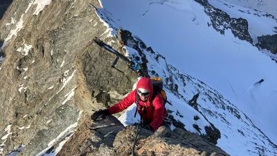 Climber with helmet and rope on a snow-covered mountain ridge in the Alps.