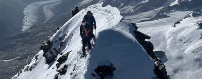 Mountaineers with helmets and ropes on a snow-covered ridge in an alpine mountain landscape.