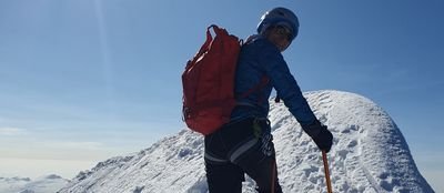 Person with helmet and backpack climbing on a snow-covered mountain peak.