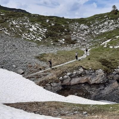 Im Vordergrund ist ein Schneefeld und dahinter ein schneefreier Wanderweg mit einigen Personen