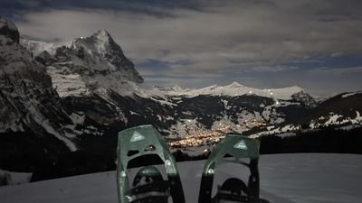 Snowshoes in the foreground, mountain landscape, and illuminated valley in the background at night.